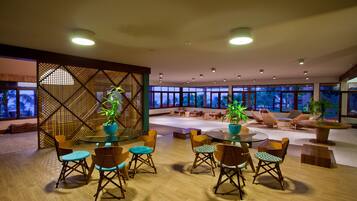 A spacious lounge area with a round table and chairs, a wooden partition with a lattice design, and large windows offering a view of the night sky.