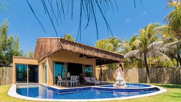 A modern house with a pool, a thatched roof, and palm trees.