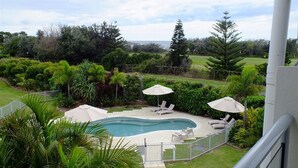 Una piscina con sillones de descanso y sombrillas, rodeada de exuberante vegetación y vistas al paisaje.