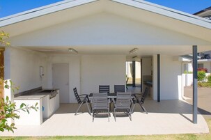 An outdoor covered patio with a dining table and chairs, a built-in grill, and a view of the adjacent house.