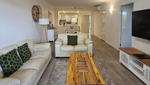 Una sala de estar con sofá, mesa de centro, televisor y una cocina al fondo.