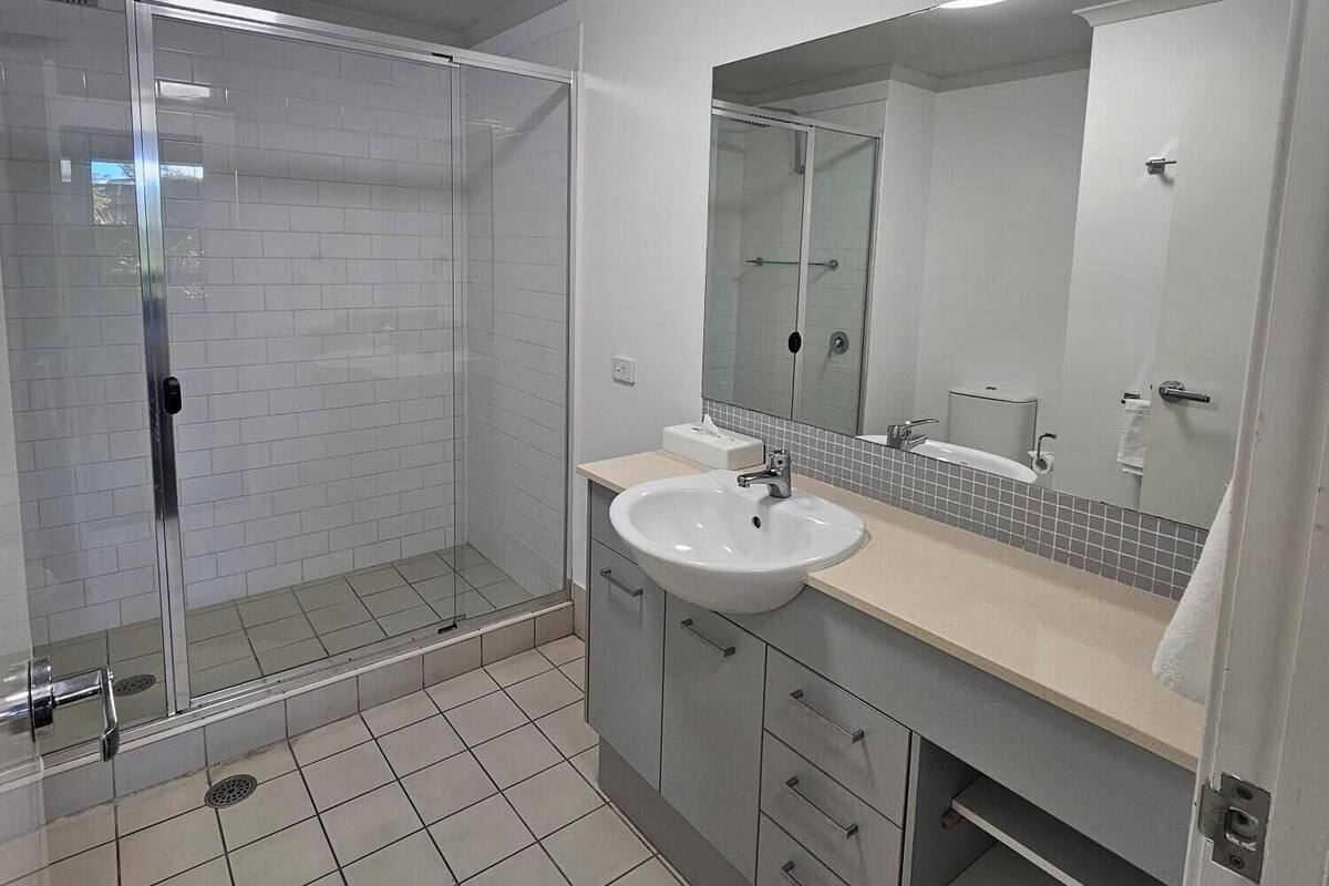 A modern bathroom with a glass shower enclosure, a sink with a mirror, and tiled flooring.