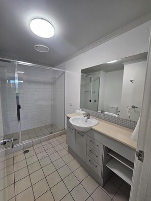 A modern bathroom with a glass shower enclosure, a sink with a mirror, and tiled flooring. - Pacific Marina Apartments (Coffs Harbour)