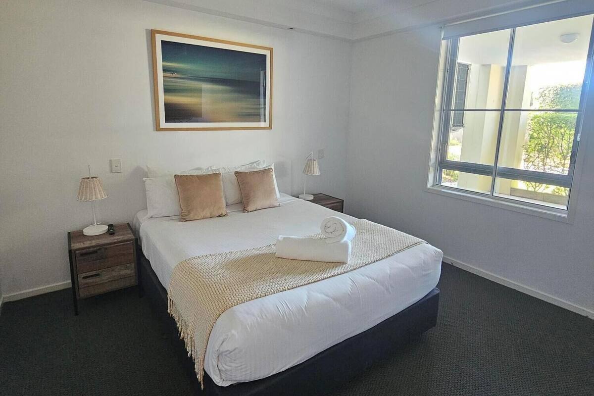 A hotel room with a large bed, a ceiling fan, a window with a view, and a painting on the wall.