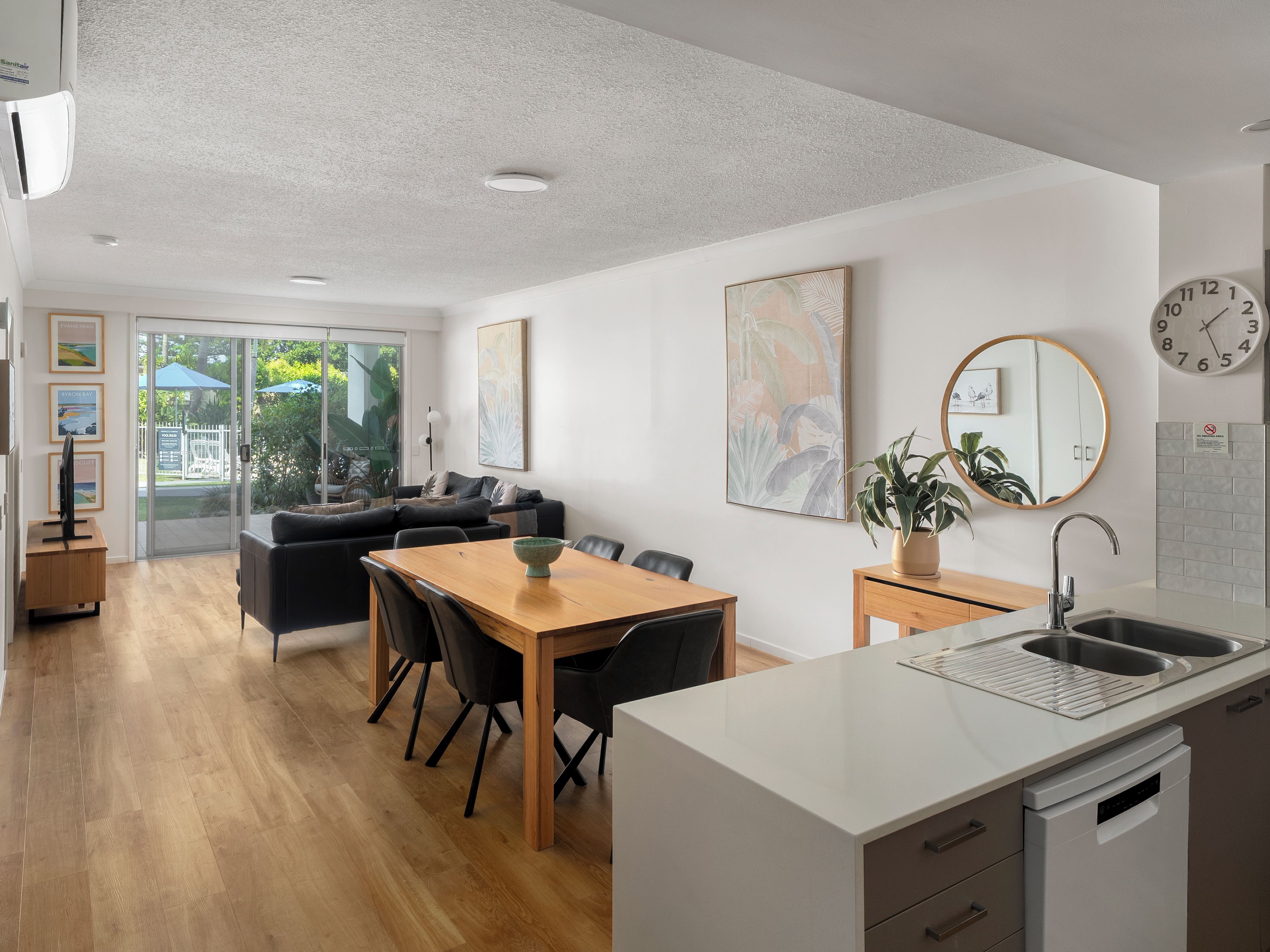 A modern kitchen with a dining area, a built-in dishwasher, and a large window overlooking a garden.