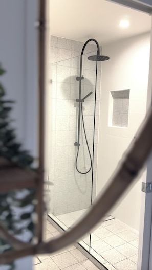 A glass-enclosed shower with a handheld showerhead and a wall-mounted faucet.