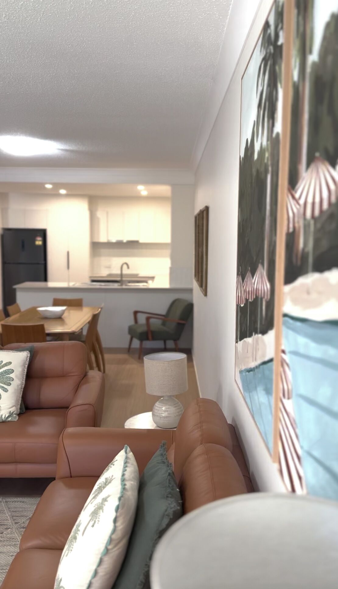 Una sala de estar moderna con un sofá de cuero marrón, una mesa de comedor y una cocina al fondo.