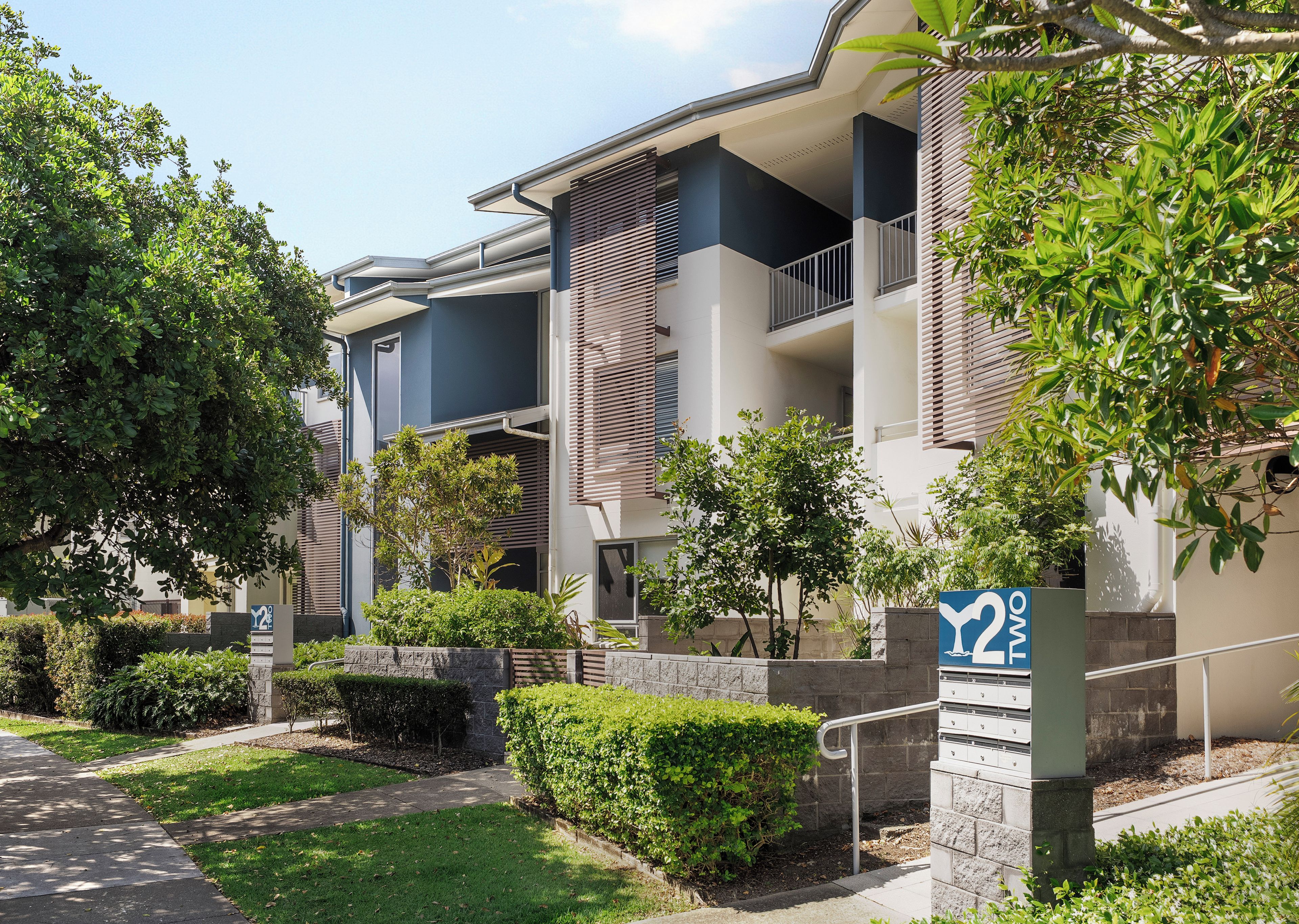 A modern apartment building with balconies, a landscaped garden, and a clear sky.