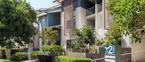 A modern apartment building with balconies, a landscaped garden, and a clear sky.