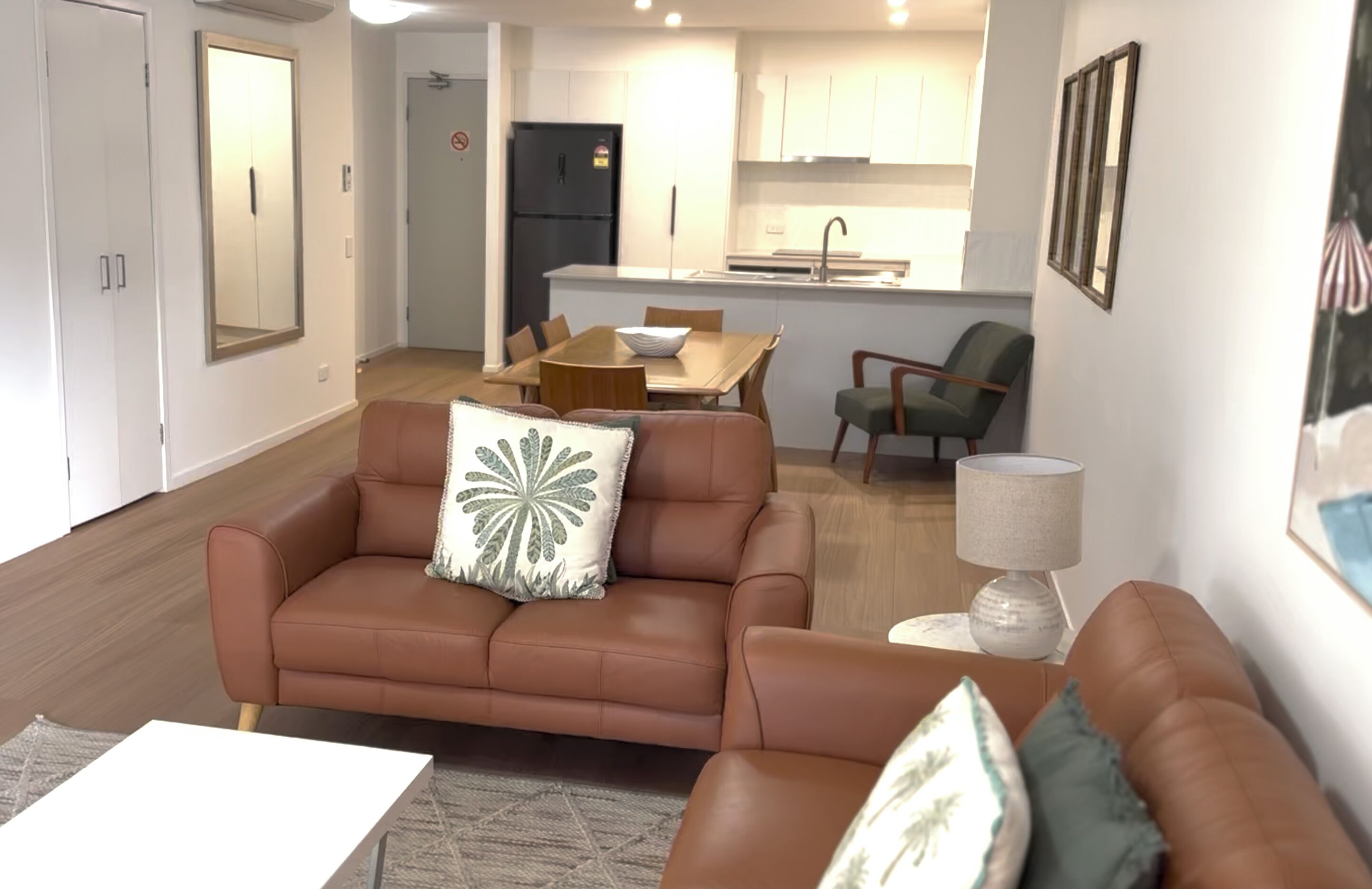 A living room with a brown sofa, a dining table, and a kitchen in the background.