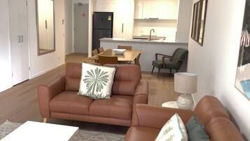 A living room with a brown sofa, a dining table, and a kitchen in the background.