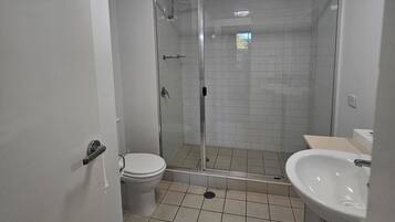 Un baño con inodoro, lavamanos, ducha con puertas de cristal y una lámpara en el techo.