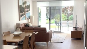 Una sala de estar moderna con comedor, un sofá, un mueble de televisión y un ventanal con vistas a zonas verdes.