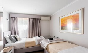 A hotel room with two beds, a large window with curtains, an air conditioning unit, and a framed painting on the wall. - Amble at Hahndorf (Hahndorf)