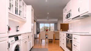 A compact kitchen with built-in appliances, a dining area with a view, and a washing machine. - Amble at Hahndorf (Hahndorf)