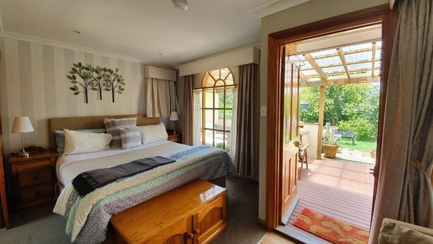 A bedroom with a bed, bedside tables, a bench, and a view of the garden through an open door. - Amble at Hahndorf (Hahndorf)
