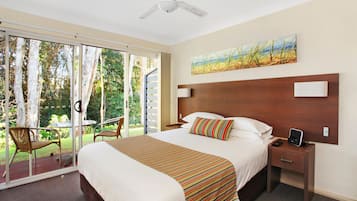 Habitación de hotel con una cama grande, una mesita de noche con un teléfono y una tableta, una silla y vistas al exterior a través de una puerta corrediza de vidrio.
