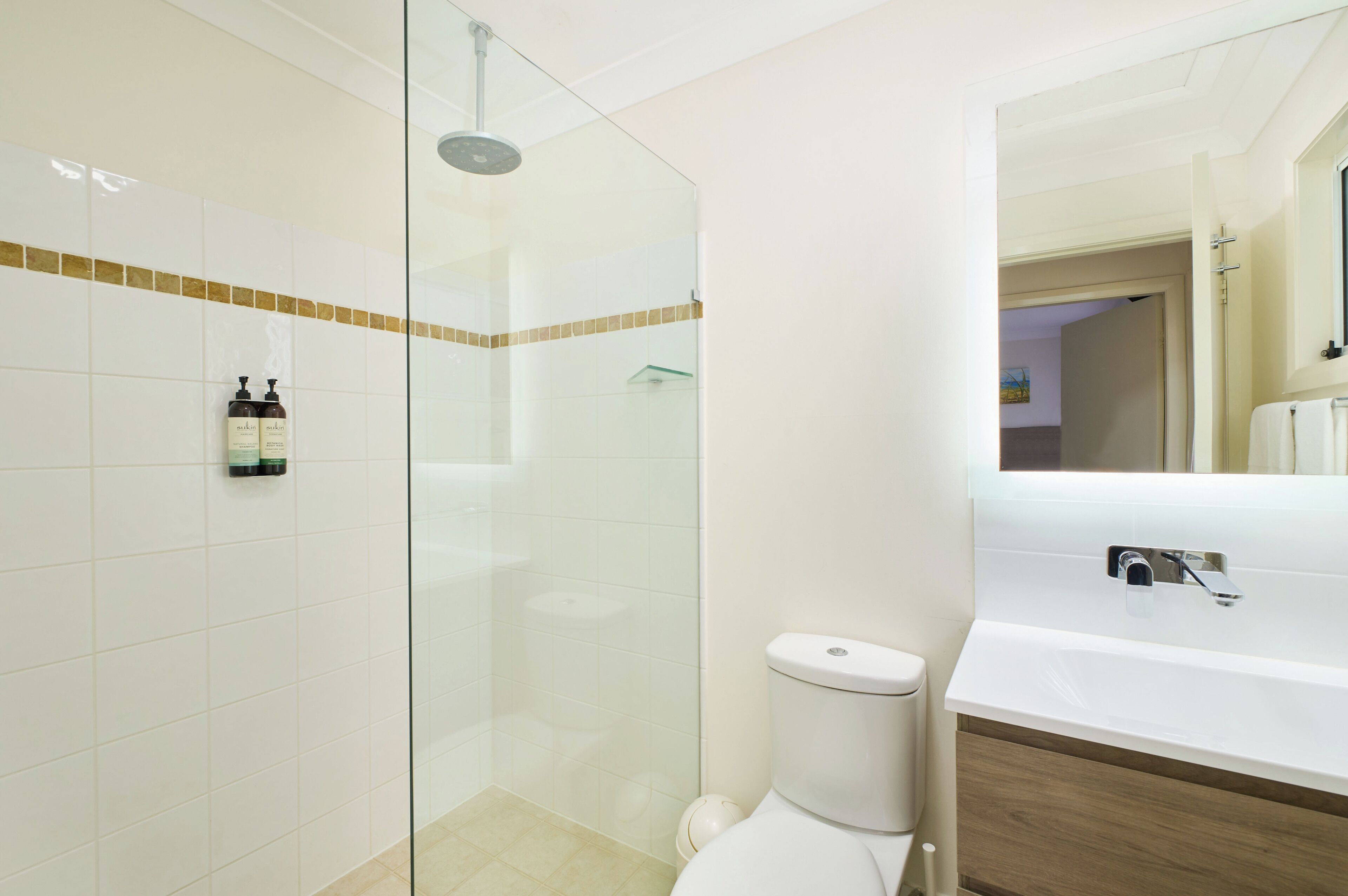 Un baño moderno con ducha envuelta en vidrio, inodoro blanco y un espejo grande sobre el lavabo.