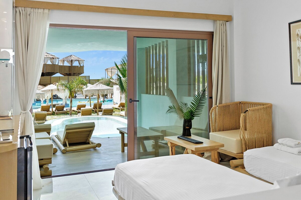 Une chambre d’hôtel avec un lit, un bureau, une chaise, une plante en pot et une vue sur l’espace piscine.