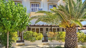 Un edificio de varios pisos con balcones, una palmera y varios arbustos.