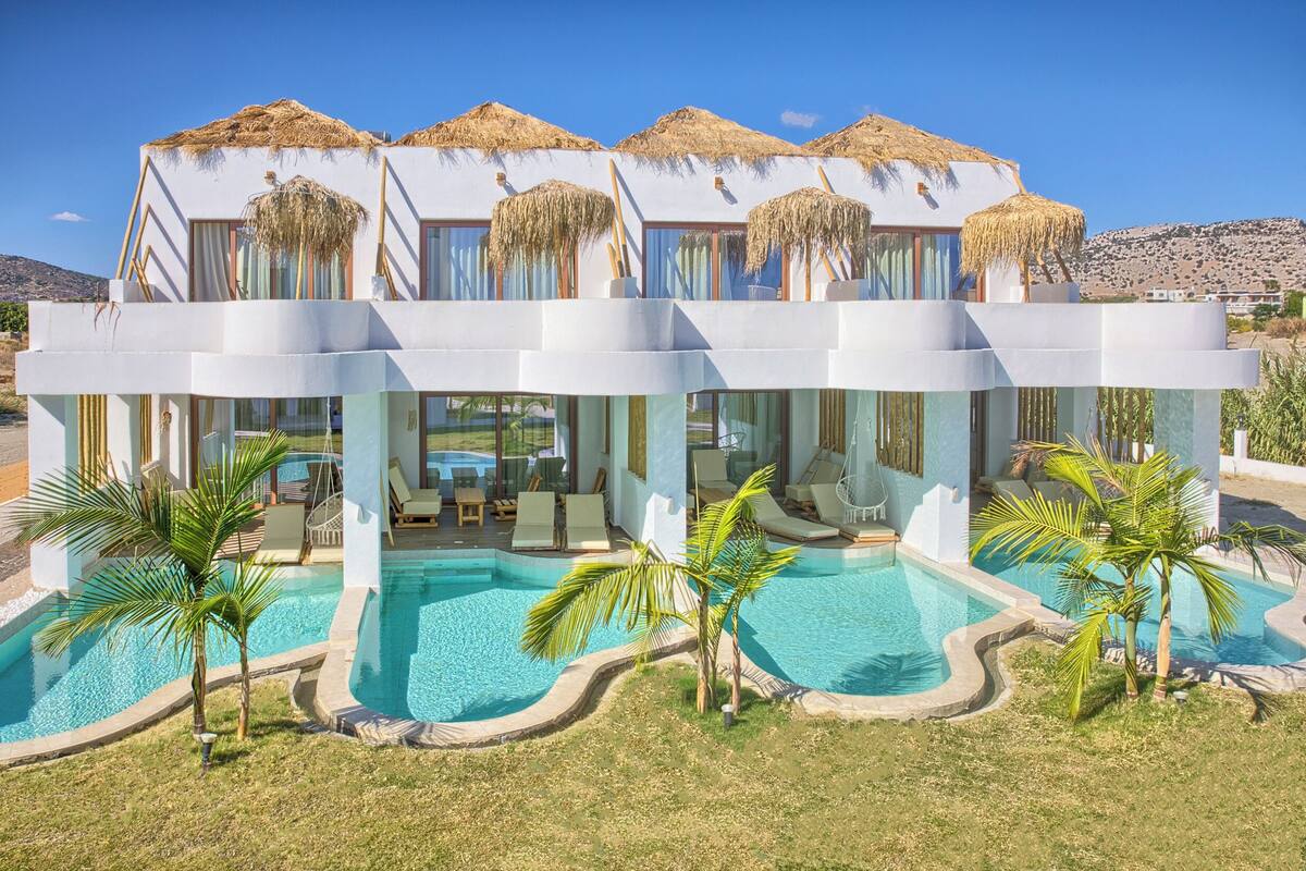 A modern resort with a pool, outdoor seating, and thatched-roof structures.