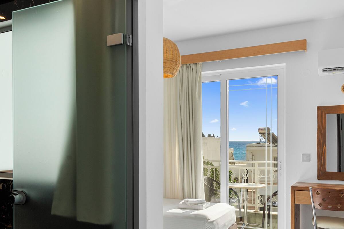 A modern hotel room with a bed, a desk, and a view of the sea.