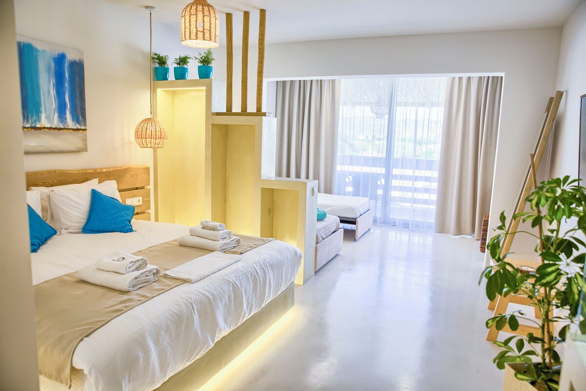 A hotel room with a bed, bedside tables, a desk, a chair, a window with curtains, and a view of the outside.