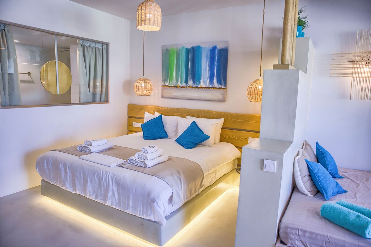 A modern hotel room with a large bed, a bedside table, a mirror, and a painting on the wall.