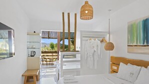 A modern hotel room with a bed, a wooden bench, a hanging light fixture, and a view of the outdoors.