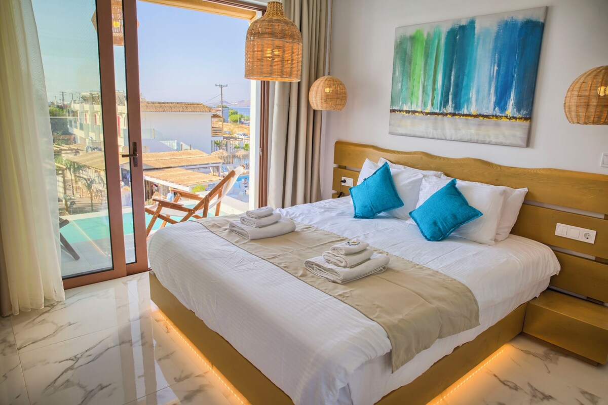 A hotel room with a bed, a painting, and a view of the sea.