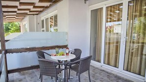 A covered outdoor seating area with wicker chairs and a round table, a bottle of wine, and a pineapple.