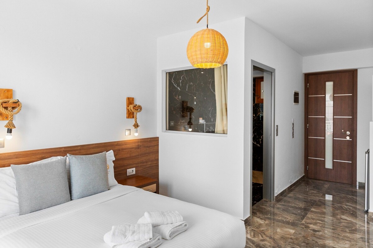 A hotel room with a bed, bedside lamps, a mirror, a door, and a hallway.