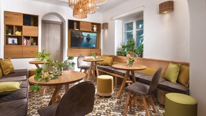 Ein modernes Wohnzimmer mit einem runden Holztisch, bequemen Sitzmöglichkeiten, einem Fernseher und einem geometrisch gemusterten Boden.
