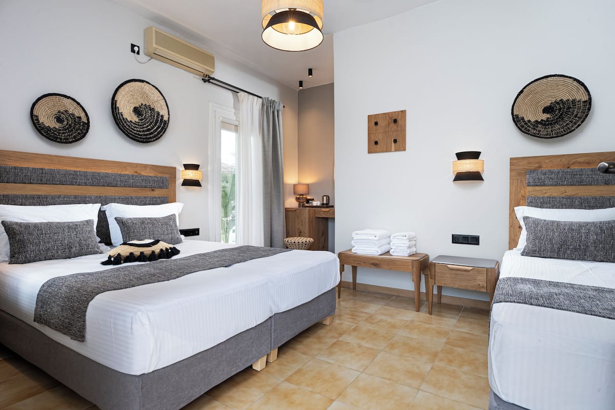 Habitación de hotel moderna con dos camas, cabecero de madera, mesita de noche con lámpara y decoración en la pared.
