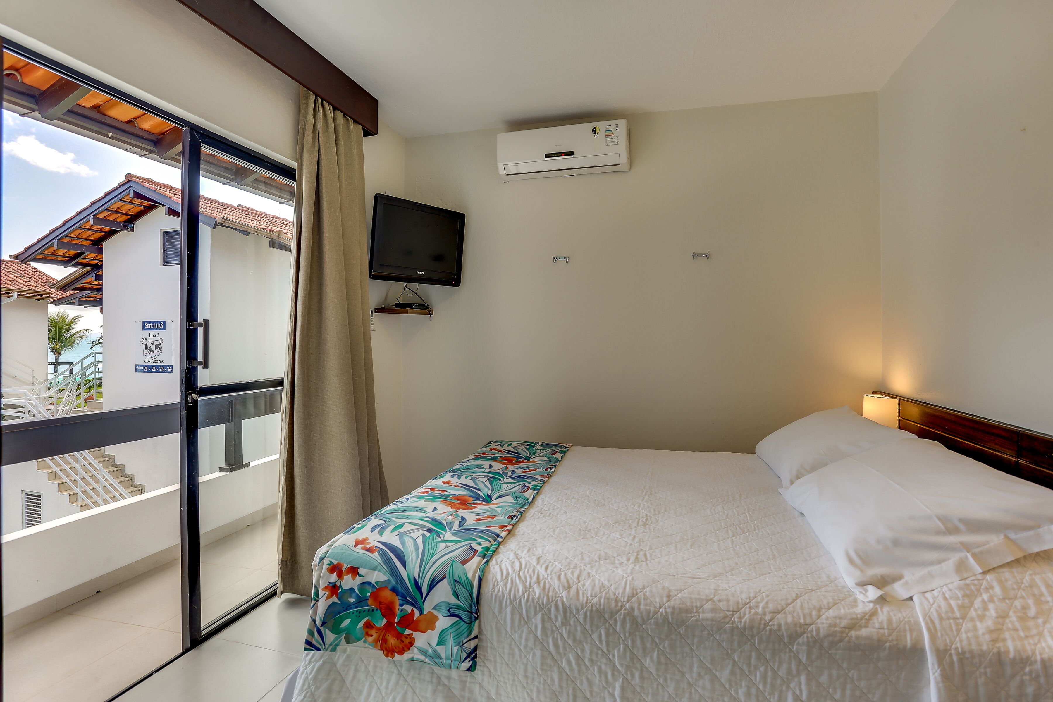 Ein Hotelzimmer mit Bett, Fernseher, Klimaanlage und einem Balkon mit Ausblick.