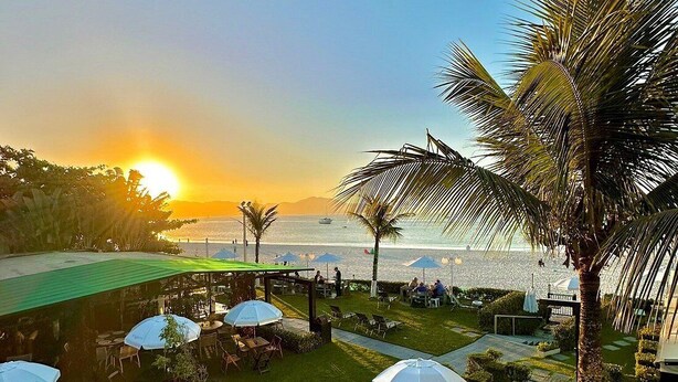 A patio area with outdoor seating, umbrellas, and a view of the sea at sunset. - Hotel Sete Ilhas (Florianópolis)