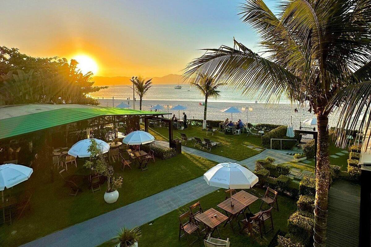 A patio area with outdoor seating, umbrellas, and a view of the sea at sunset.