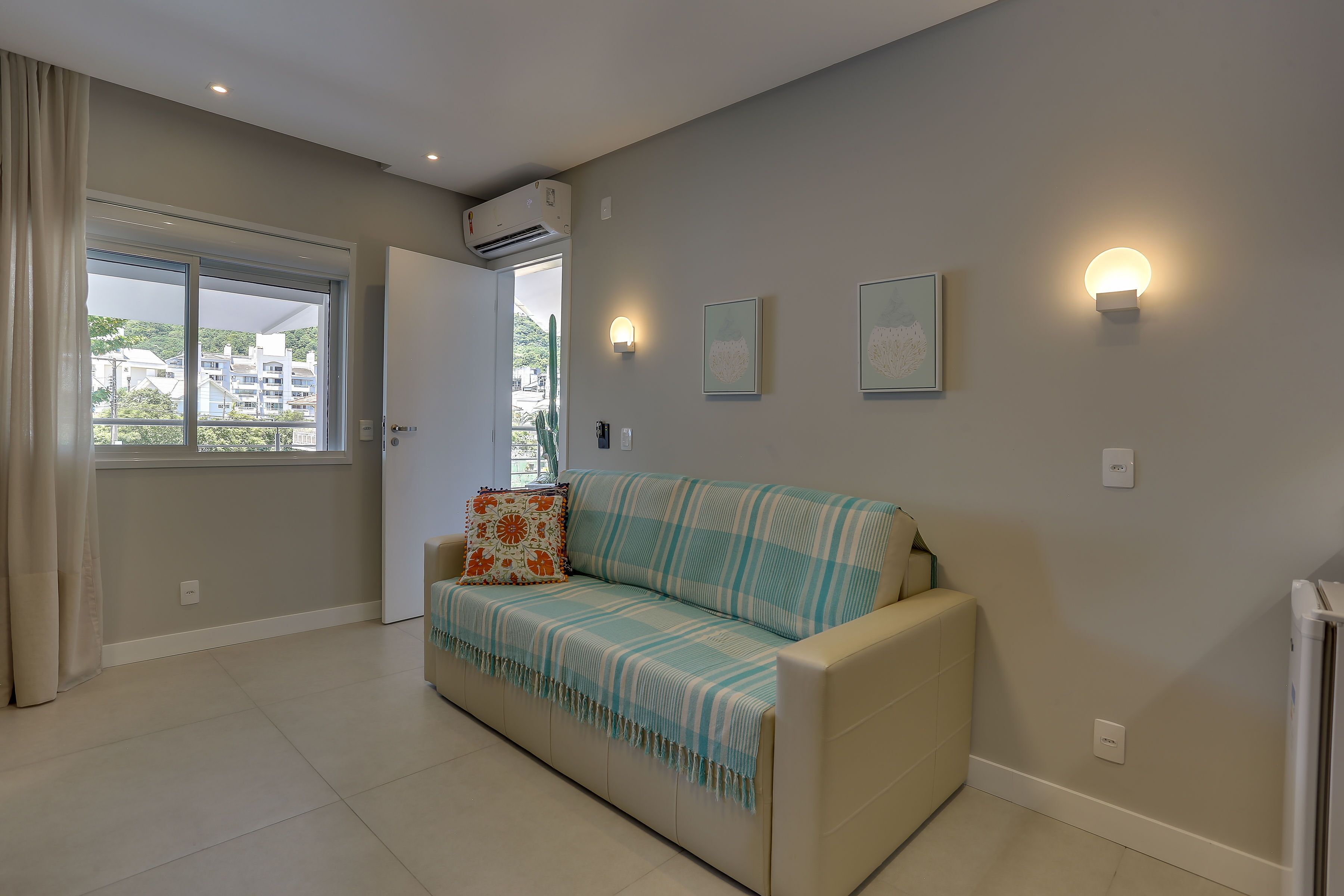 A modern living room with a beige sofa, a large window, and a wall-mounted air conditioner.