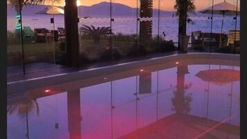 Zona de piscina con vista al océano y a las montañas al atardecer.