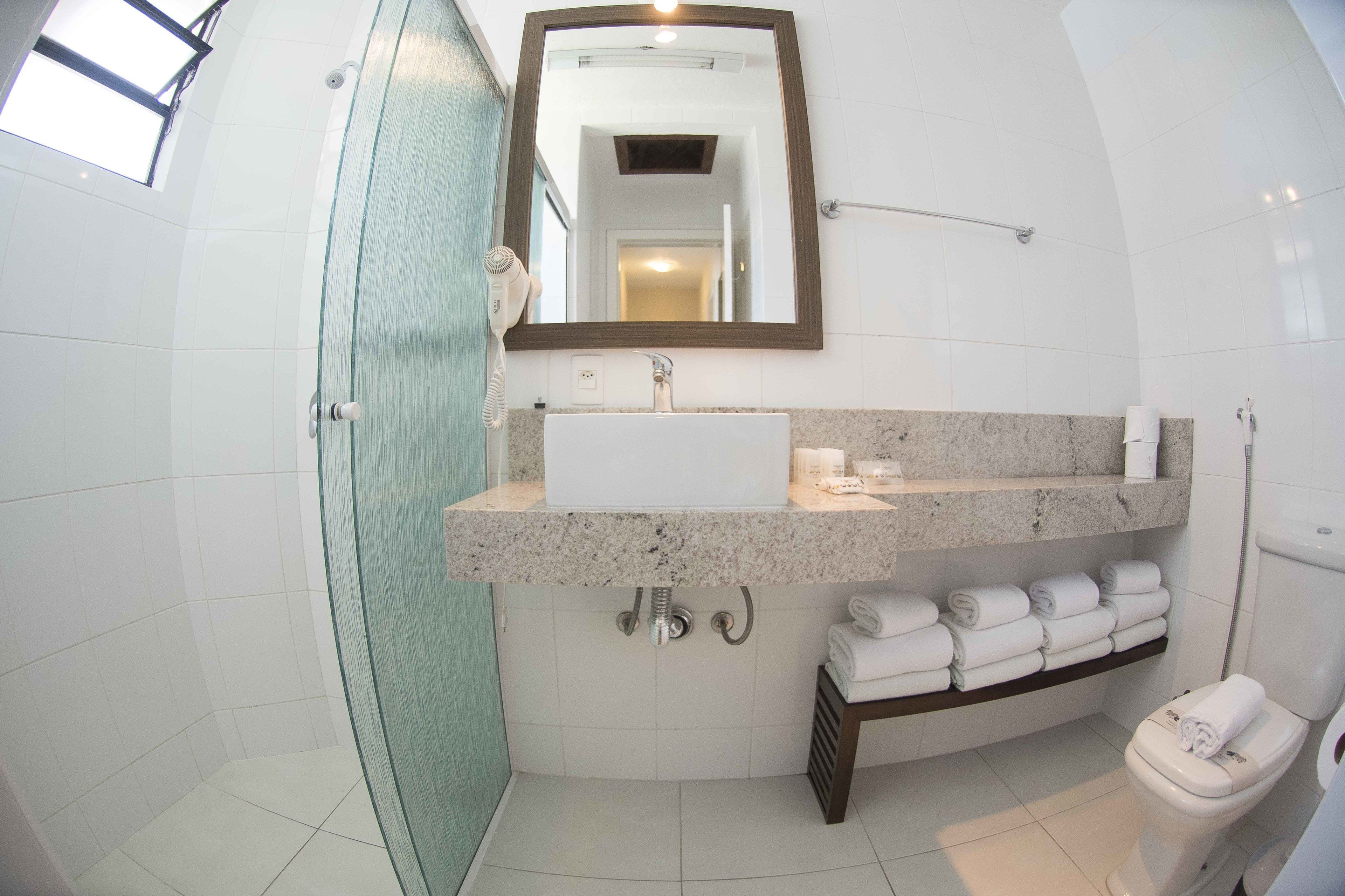 A bathroom with a glass shower enclosure, a sink with a marble countertop, a mirror above the sink, and a toilet with a towel rack.