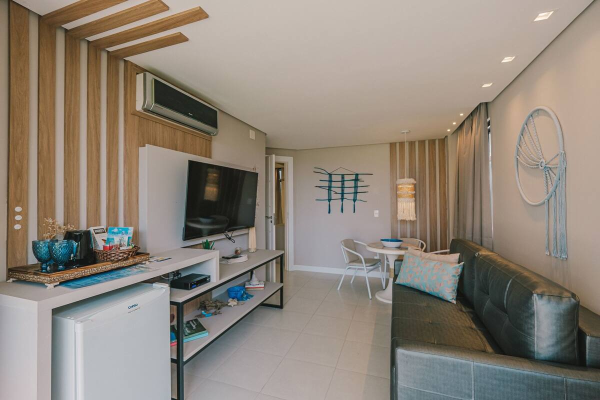A modern living room with a flat-screen TV, a sofa, a coffee table, and a dining area with chairs.