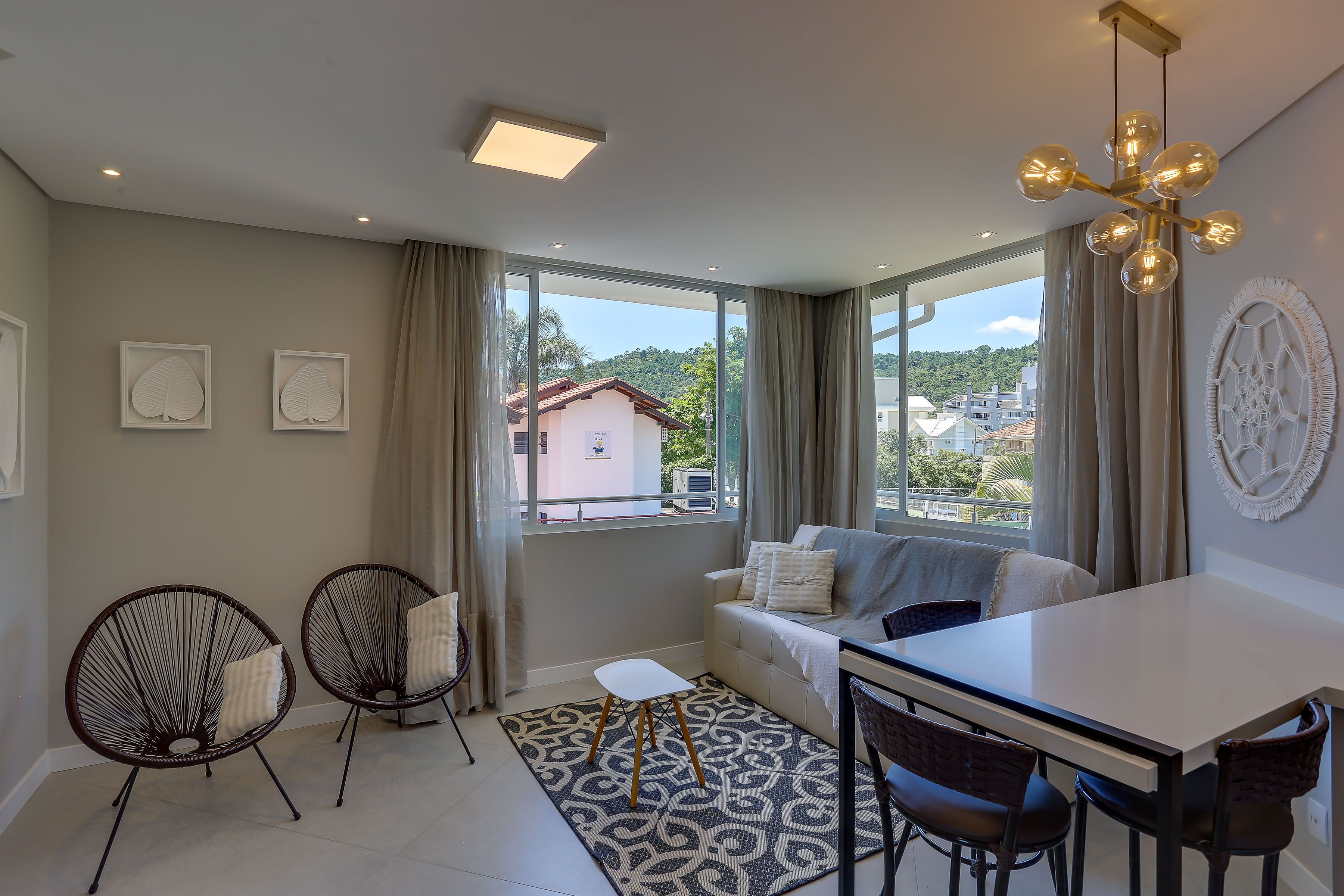 Una sala de estar moderna con un sofá, dos sillones, una mesa de comedor y un ventanal con cortinas.