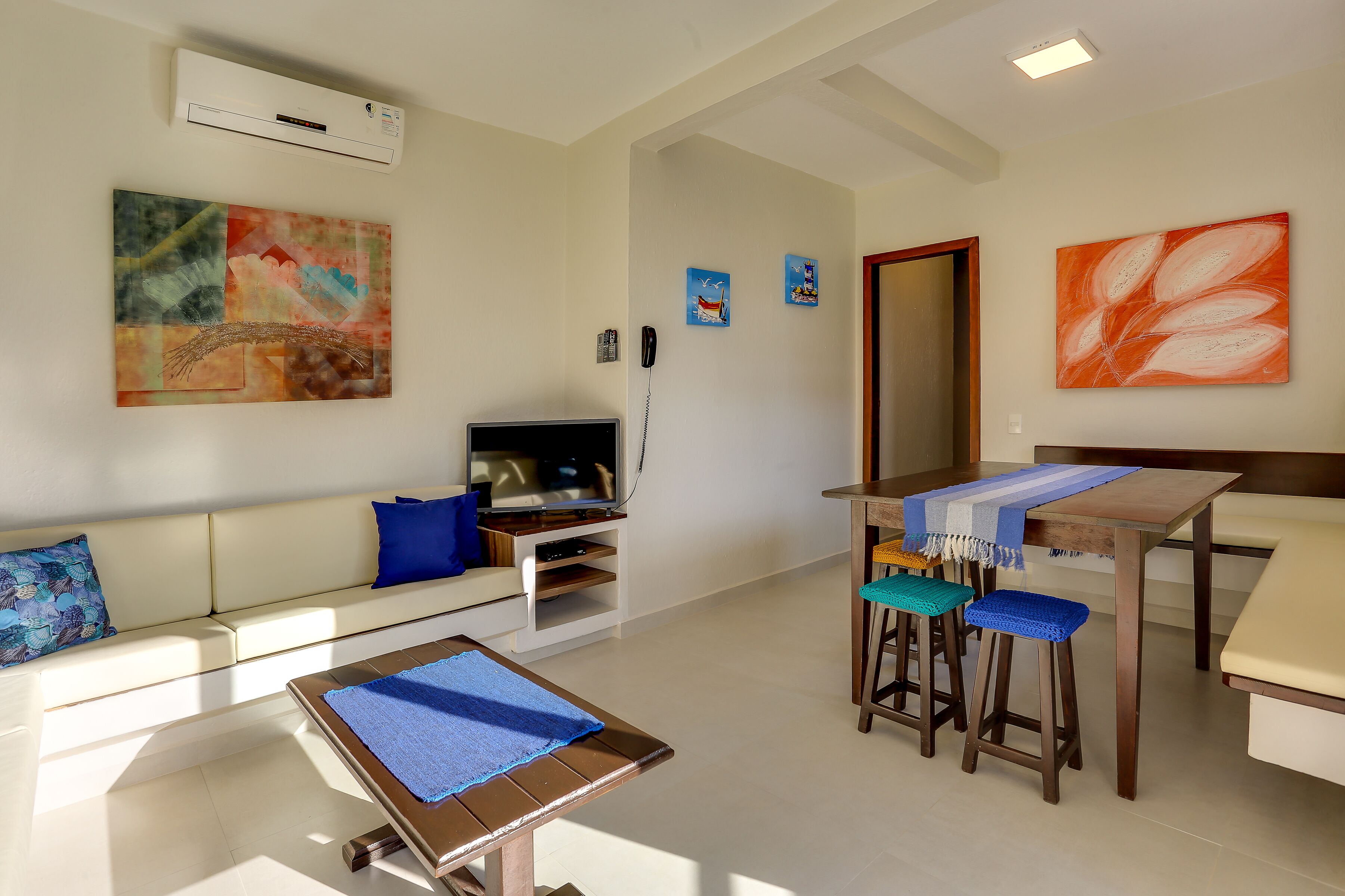 A modern living room with a sofa, a coffee table, a TV, and a dining area with stools.