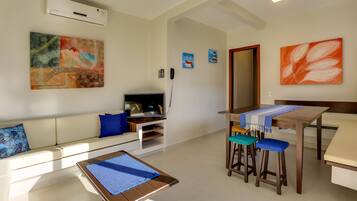 A modern living room with a sofa, a coffee table, a TV, and a dining area with stools.