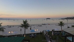 A beach view with a pool area, umbrellas, and palm trees. - Hotel Sete Ilhas (Florianópolis)