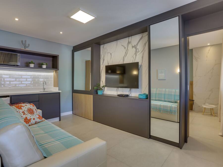A modern living room with a sofa, a flat-screen TV, a kitchen area with a microwave, and a bathroom visible through an open door.