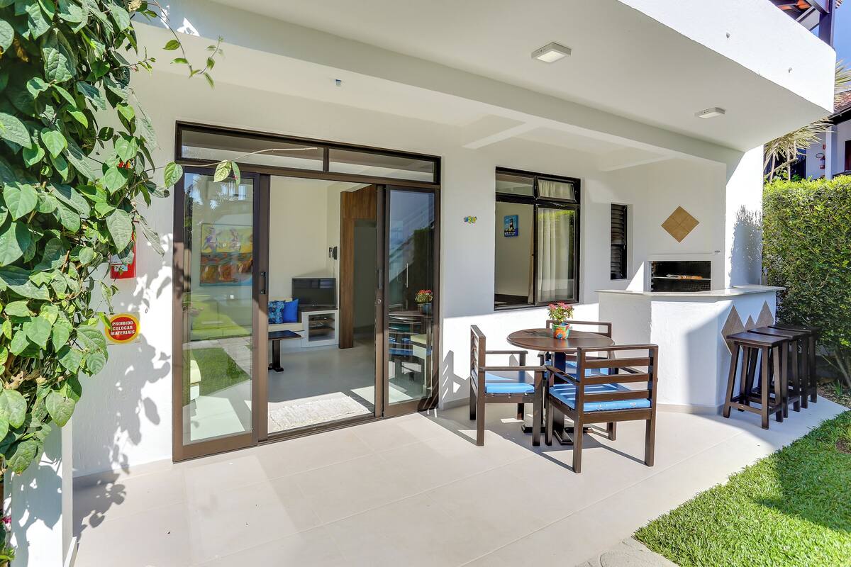 A modern outdoor patio with a glass door leading to an interior space, a round table with chairs, and a barbecue area.