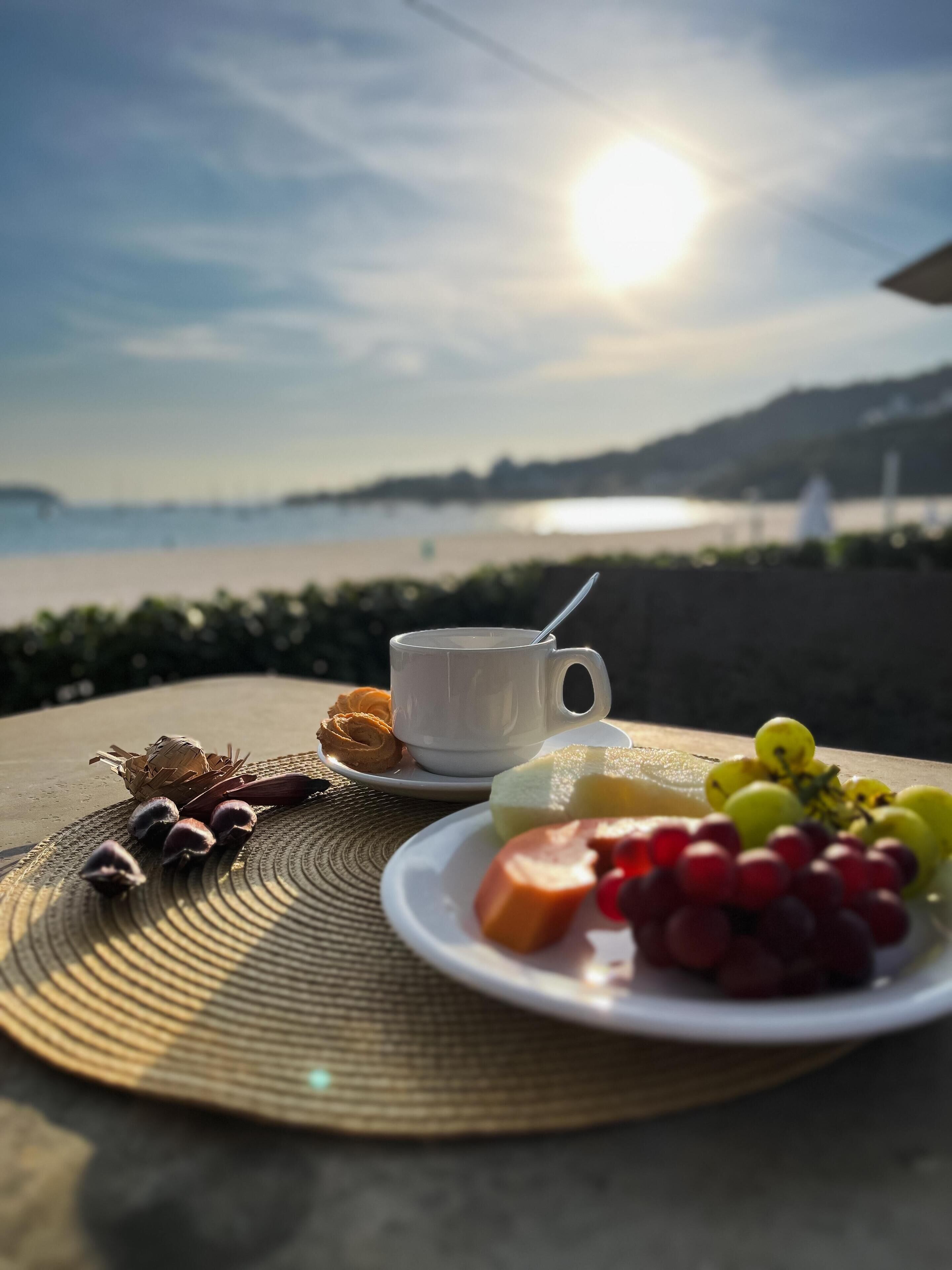 A table with a cup, plate of fruit, and a woven mat.