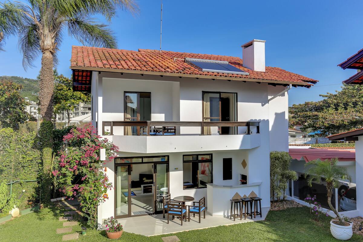 A two-story house with a red-tiled roof, solar panels, a balcony, and a patio with outdoor furniture.
