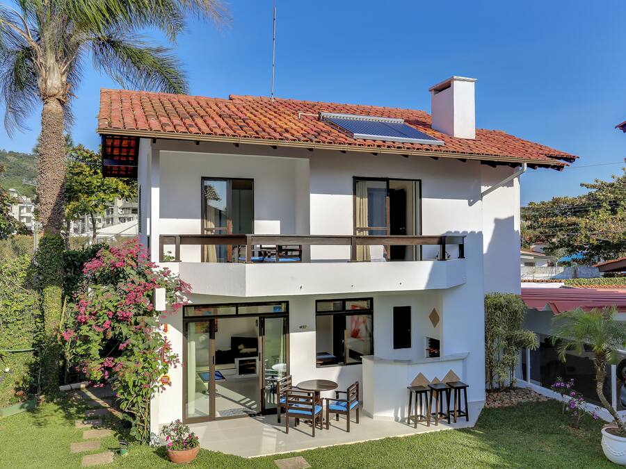 Ein zweistöckiges Haus mit rotem Ziegeldach, Solaranlage, einem Balkon und einer Terrasse mit Gartenmöbeln.